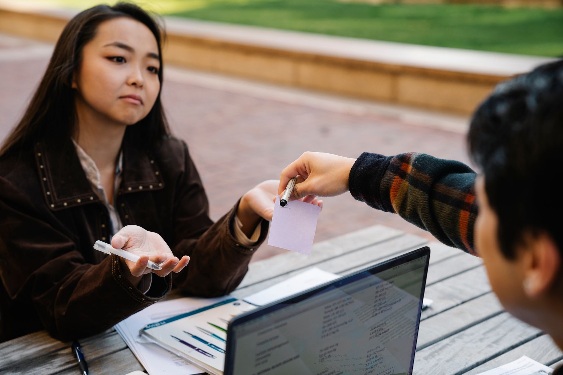 Young students exchanging notes and working together outdoors on a project.