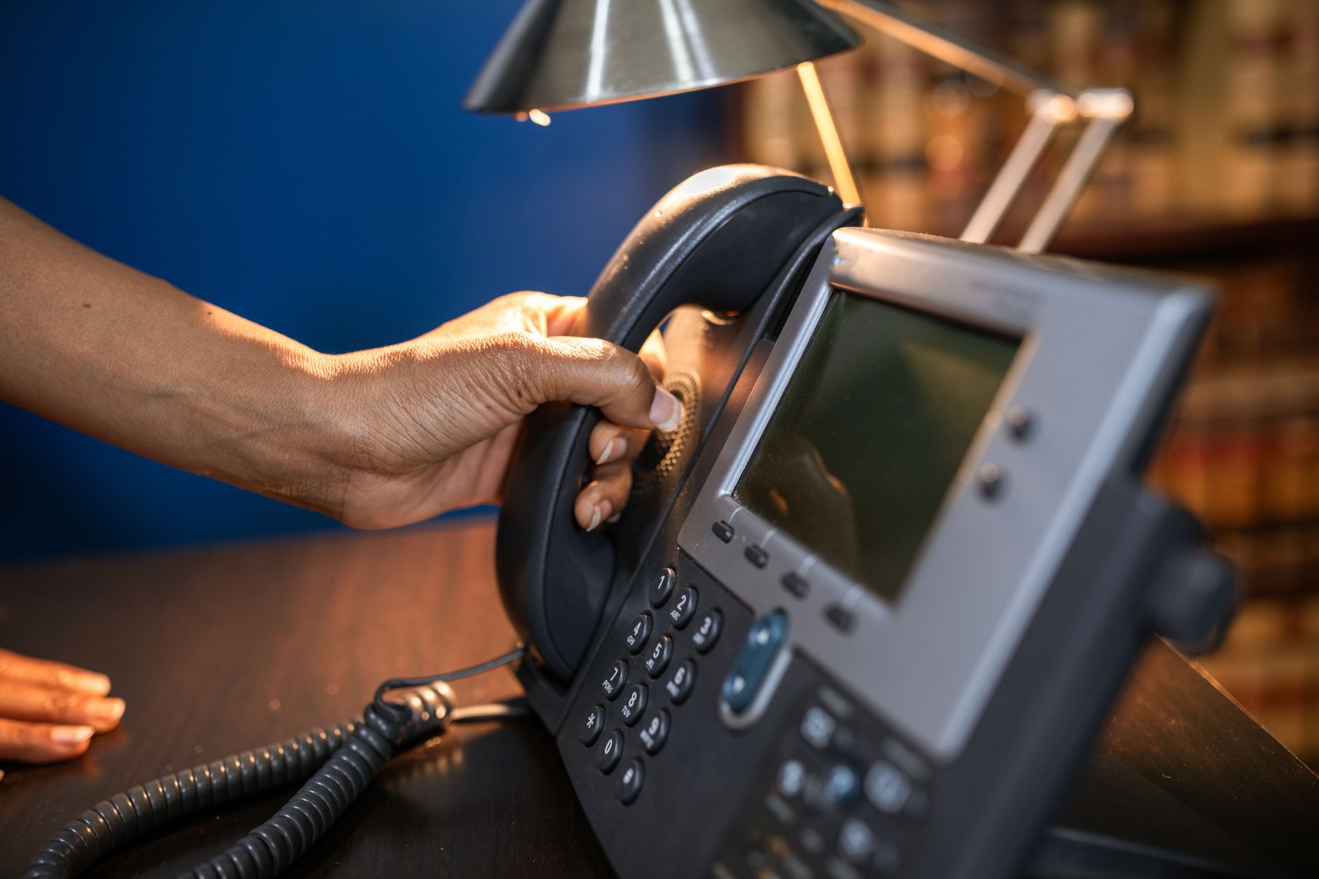A close-up image of a hand picking up a handset from an office telephone.