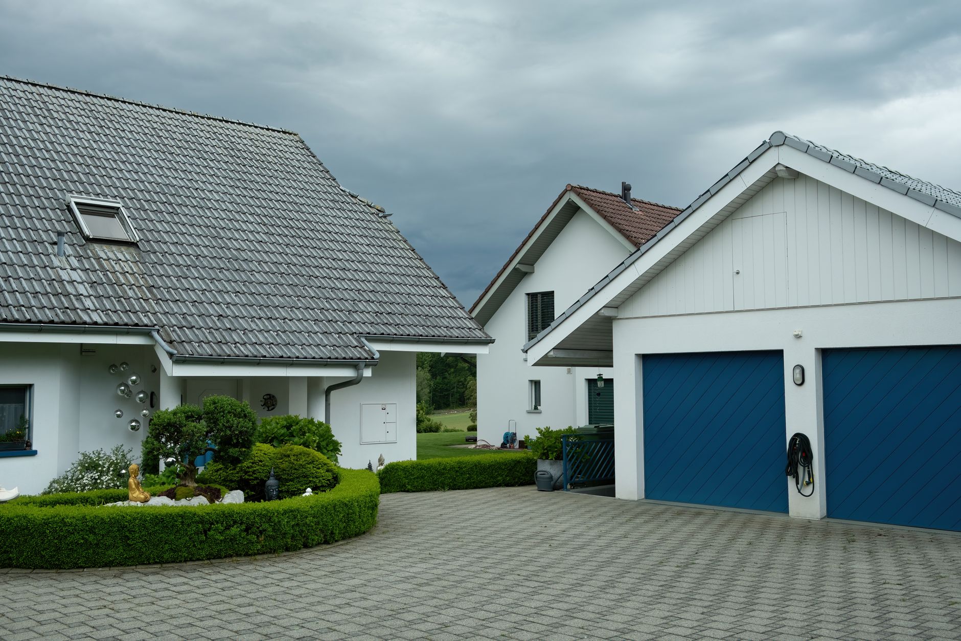 Suburban houses with blue garage doors under a cloudy sky, surrounded by greenery.