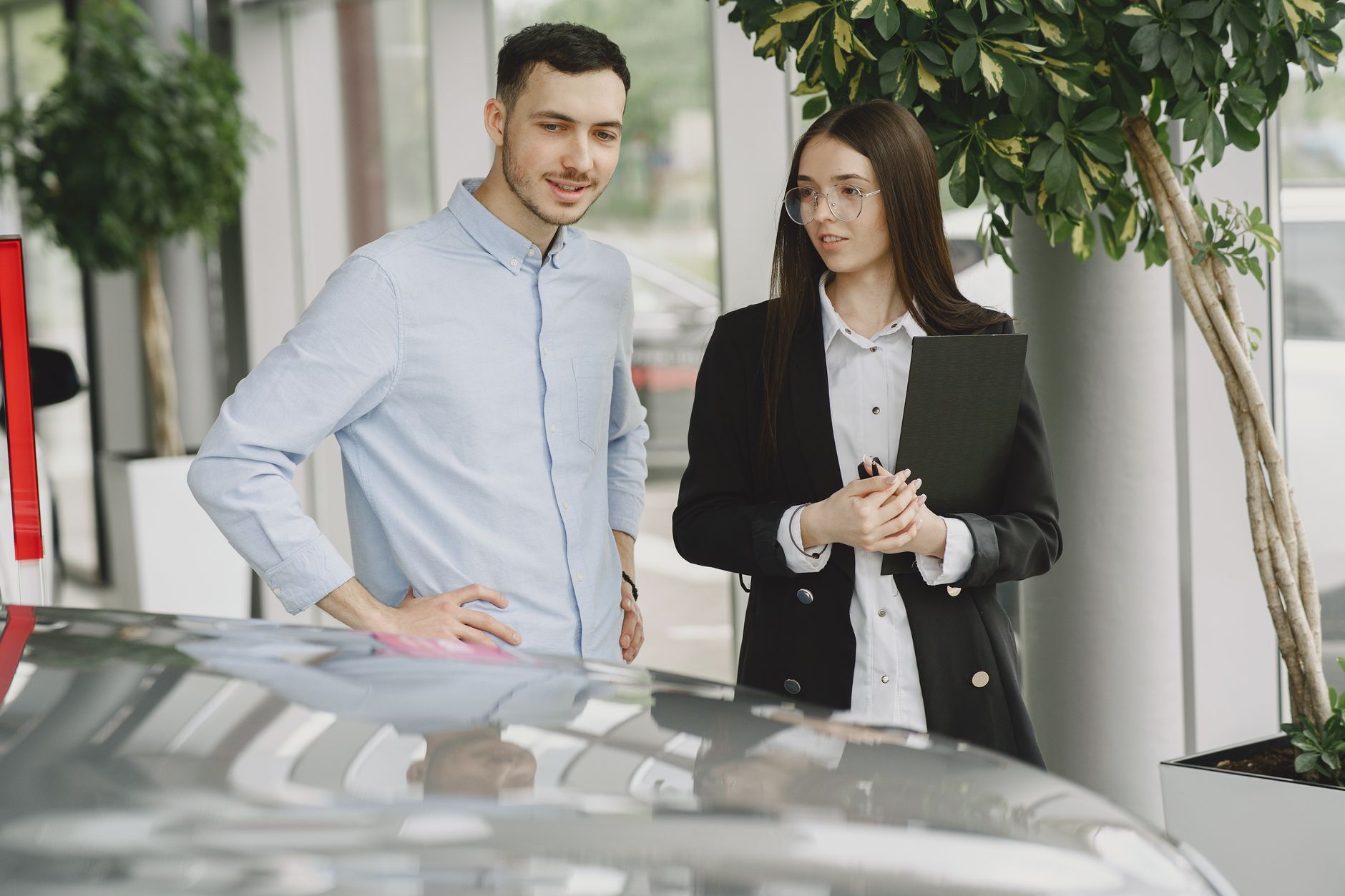Two professionals discussing business in a modern car showroom with plants around.