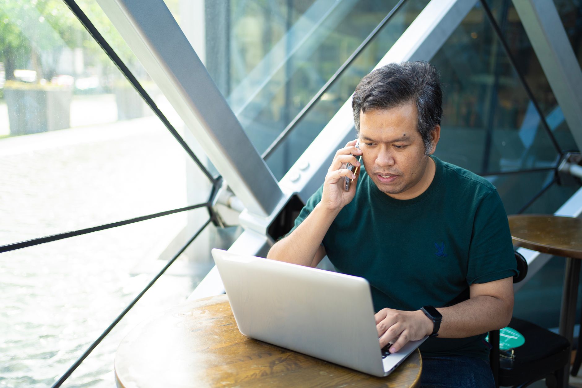 Professional multitasking on a laptop and phone at a cafe table.