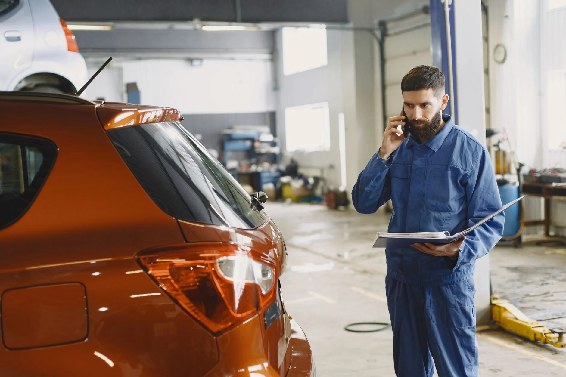 Mechanic on a phone call beside a car in an auto repair shop