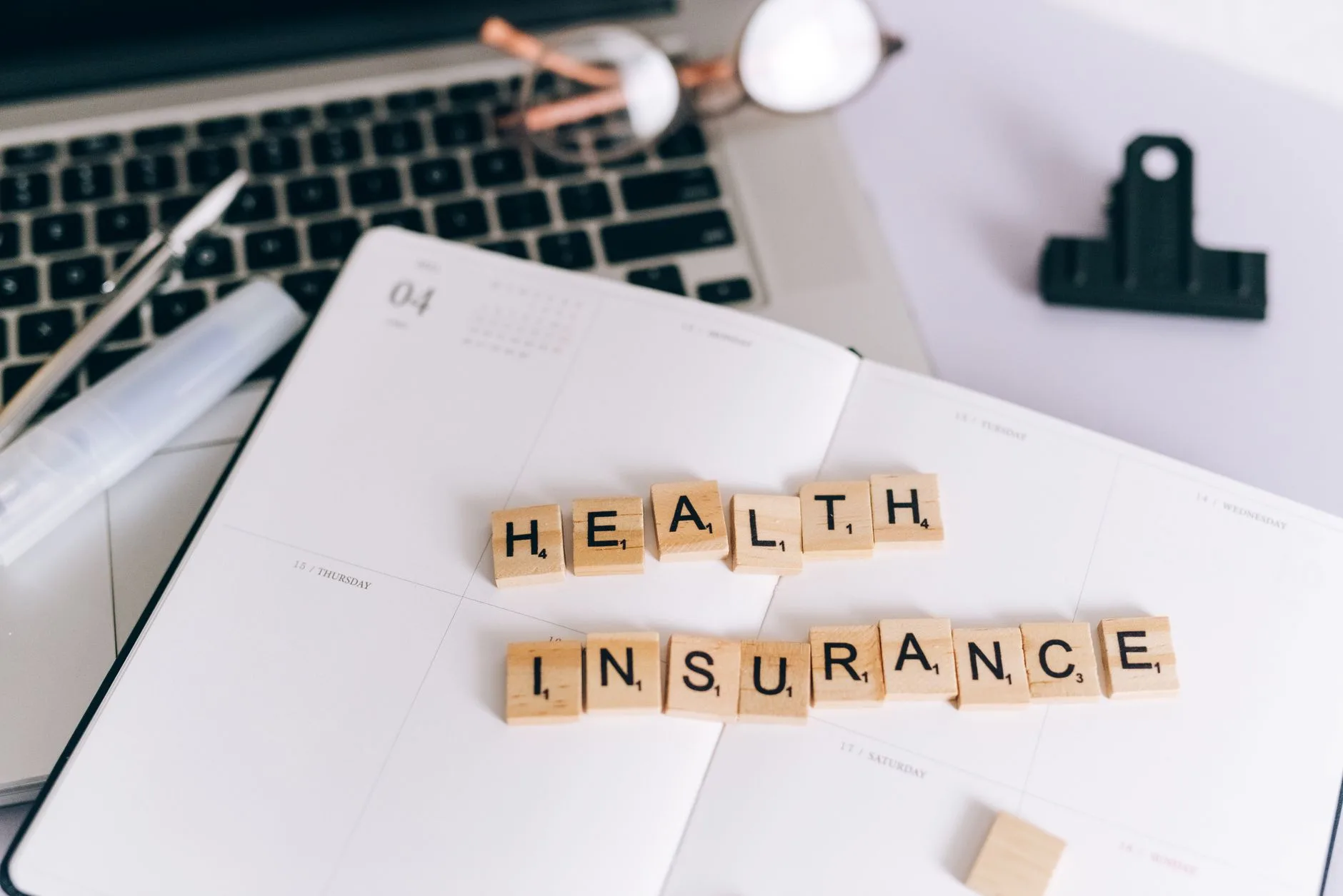 Health insurance spelled out in letter tiles beside a laptop