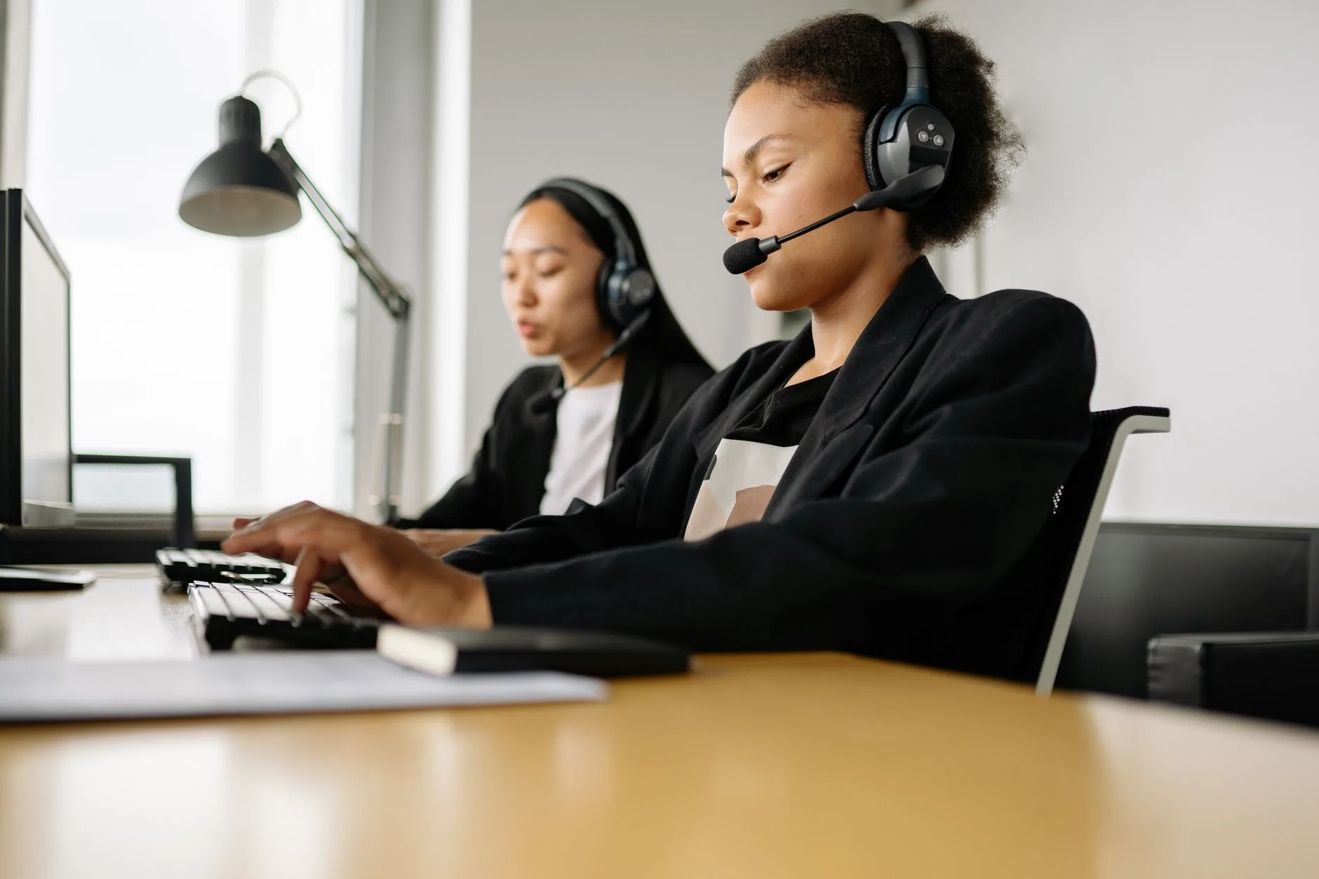 Two contact center agents wearing headsets working at computers
