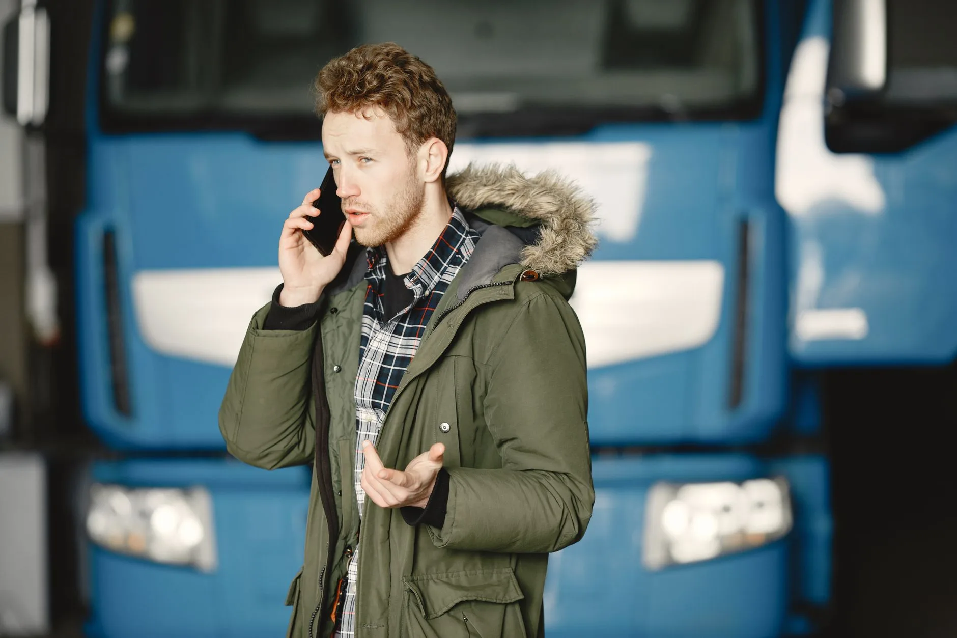 Man in a green parka talking on the phone beside a blue truck cab