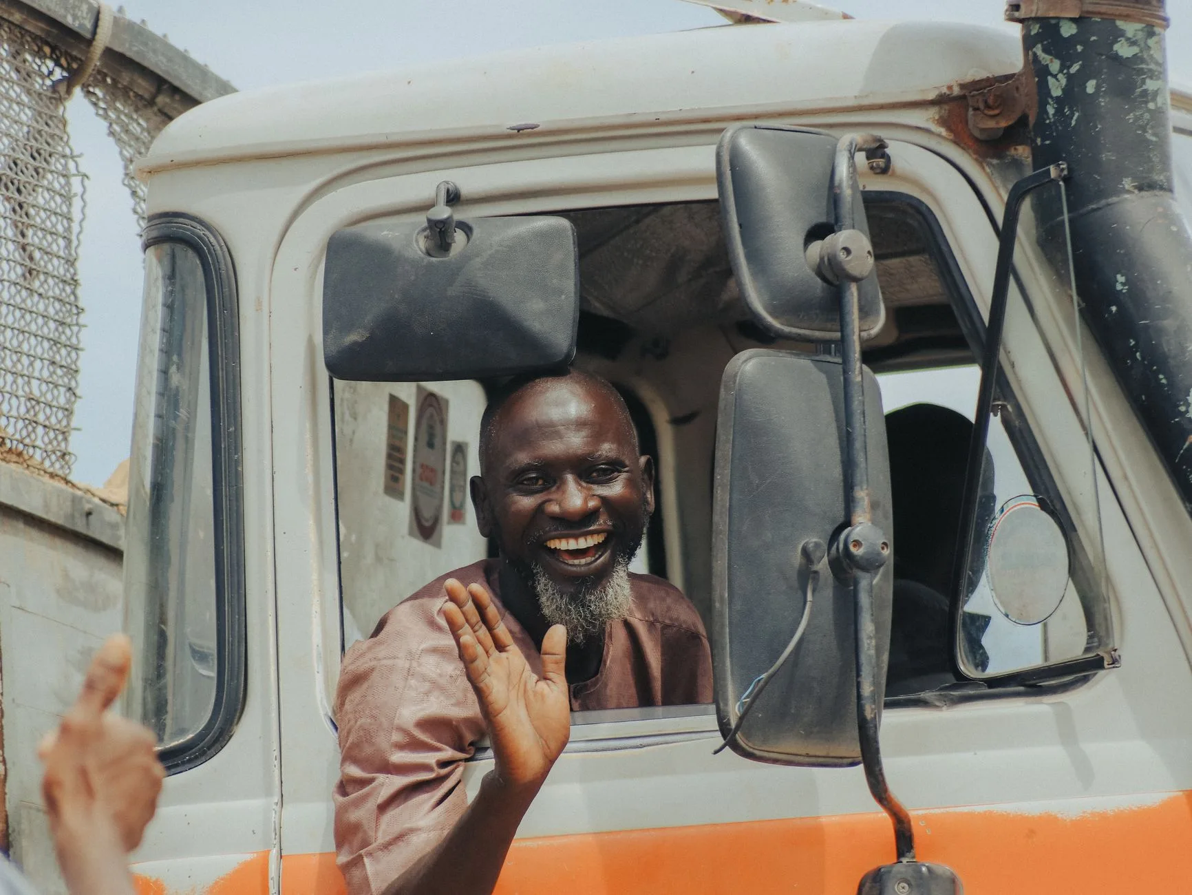 Smiling truck driver waving from the cab of a white truck