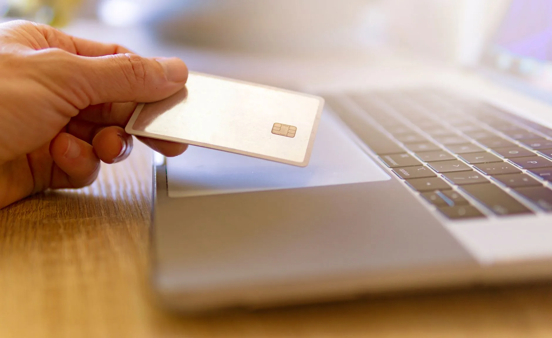 Hand holding a bank card above a laptop keyboard