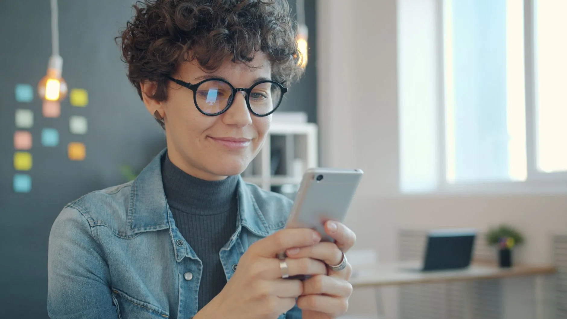 Smiling woman with glasses holding a smartphone