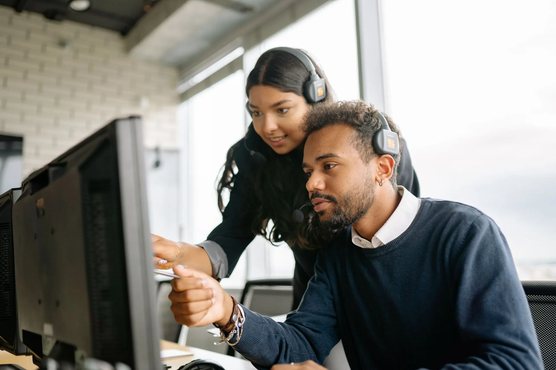 Two support staff wearing headsets looking at a computer screen together