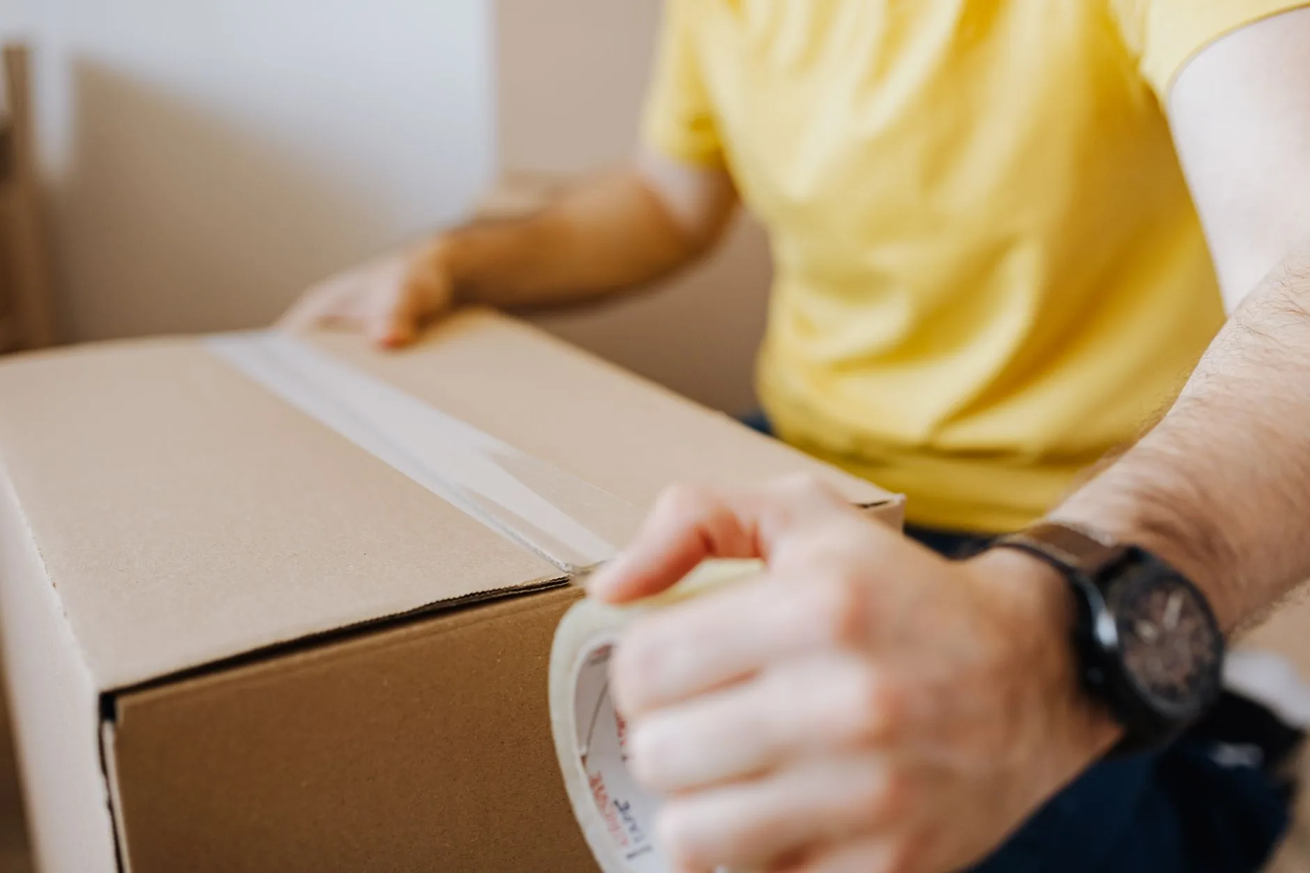 Person sealing a cardboard box with packing tape before sending it back