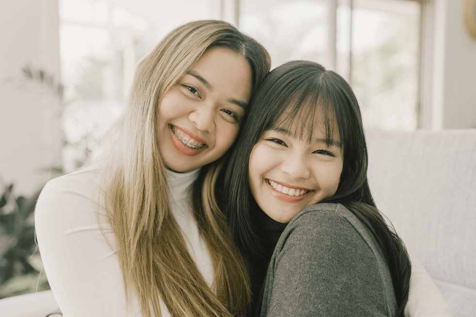 Two teenage girls show off their smiles - one with braces and the other with Invisalign clear aligners in Mountain View