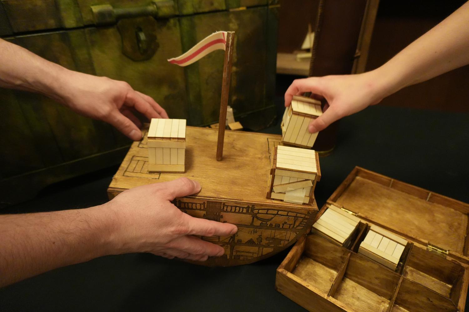 Hands loading cargo onto a handmade wooden ship