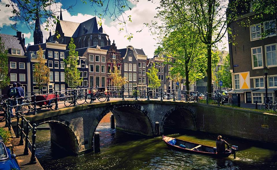 view of a canal in Amsterdam, with a person sailing a boat under a bridge