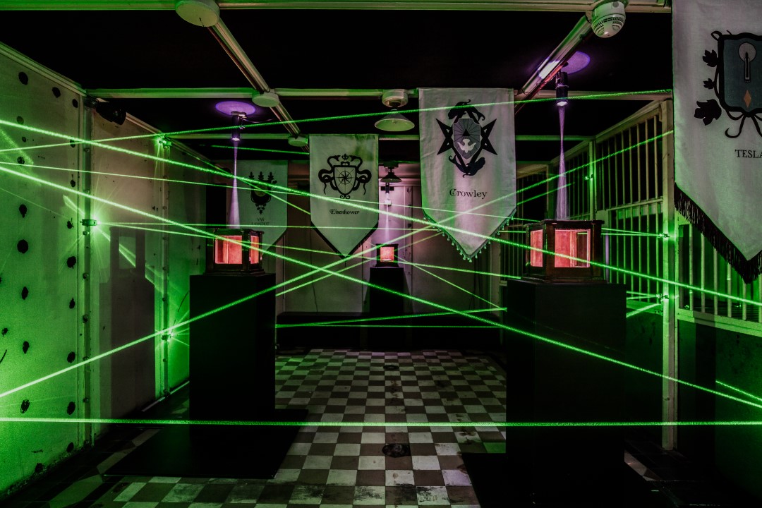 a room with four flags hanging from the ceiling, green lasers, and three red transparent boxes sitting on pedestals in the vault escape room in amsterdam
