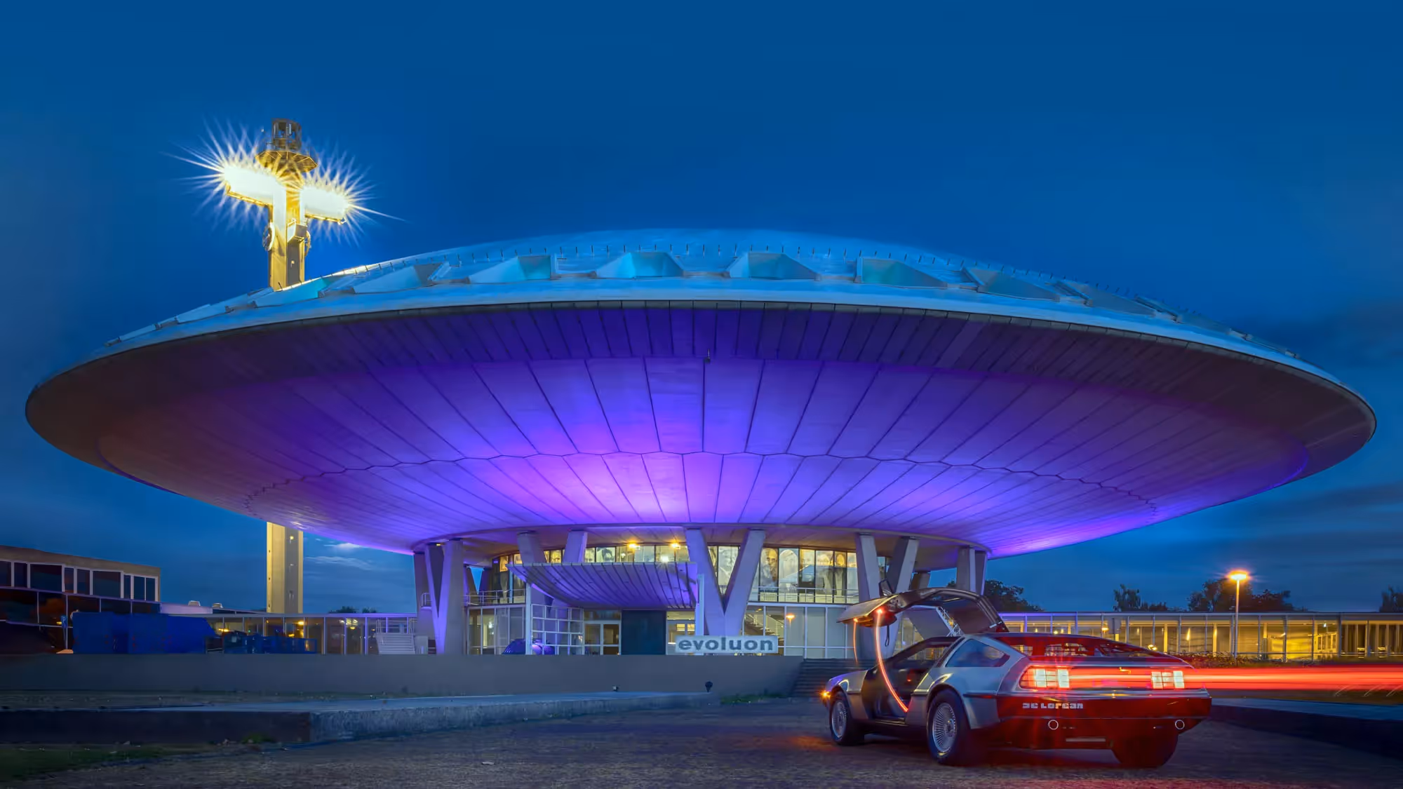The Next Nature Museum housed in the futuristic Evoluon building in Eindhoven, featuring a DeLorean car and dramatic night lighting.