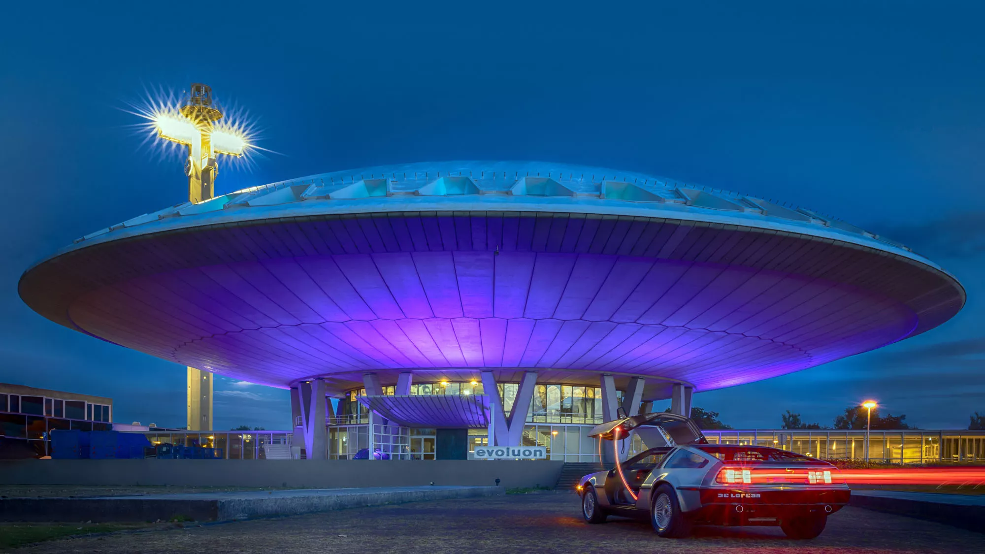The Next Nature Museum housed in the futuristic Evoluon building in Eindhoven, featuring a DeLorean car and dramatic night lighting.