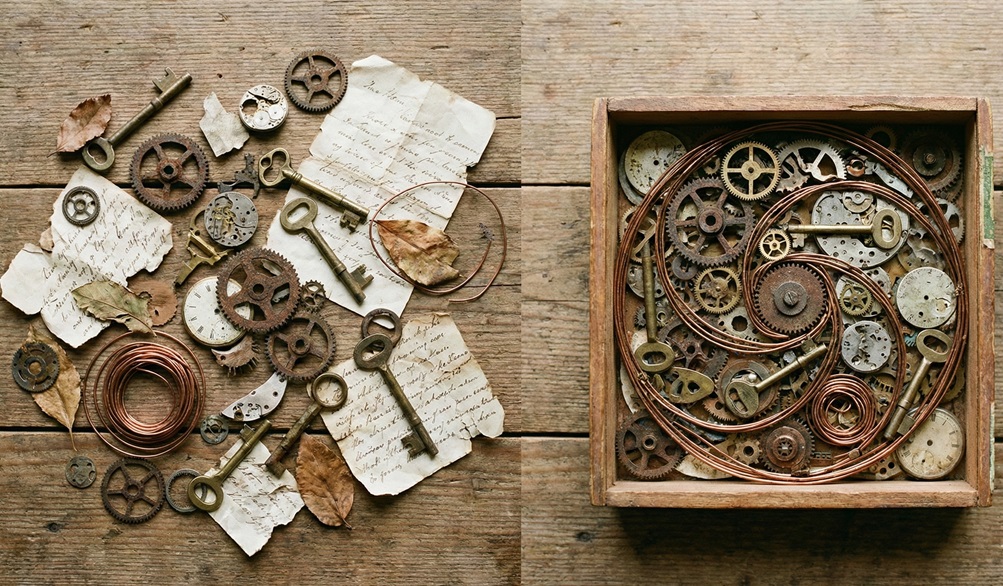 A side-by-side comparison of loose vintage escape room props: rusty gears, brass keys, and old letters, scattered on a wooden table versus being perfectly organized and spiraled within a small wooden box.