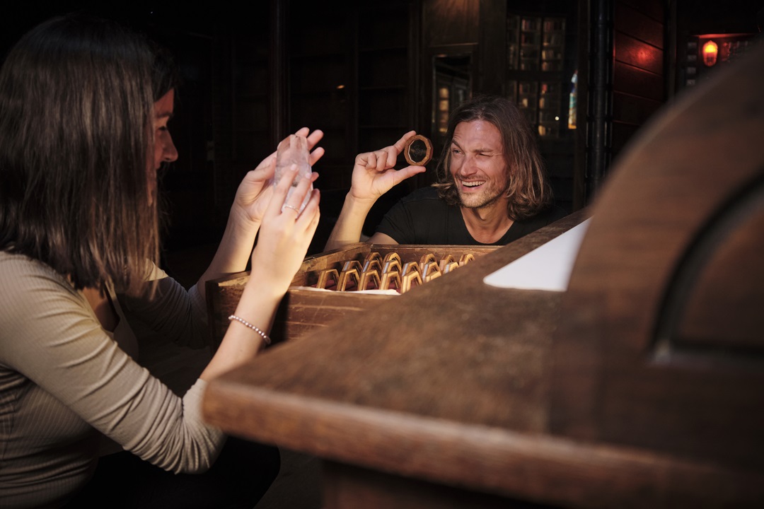 Two players smiling while examining artifacts and lenses in a wooden chest, illustrating the joy of discovery and curiosity at Sherlocked.