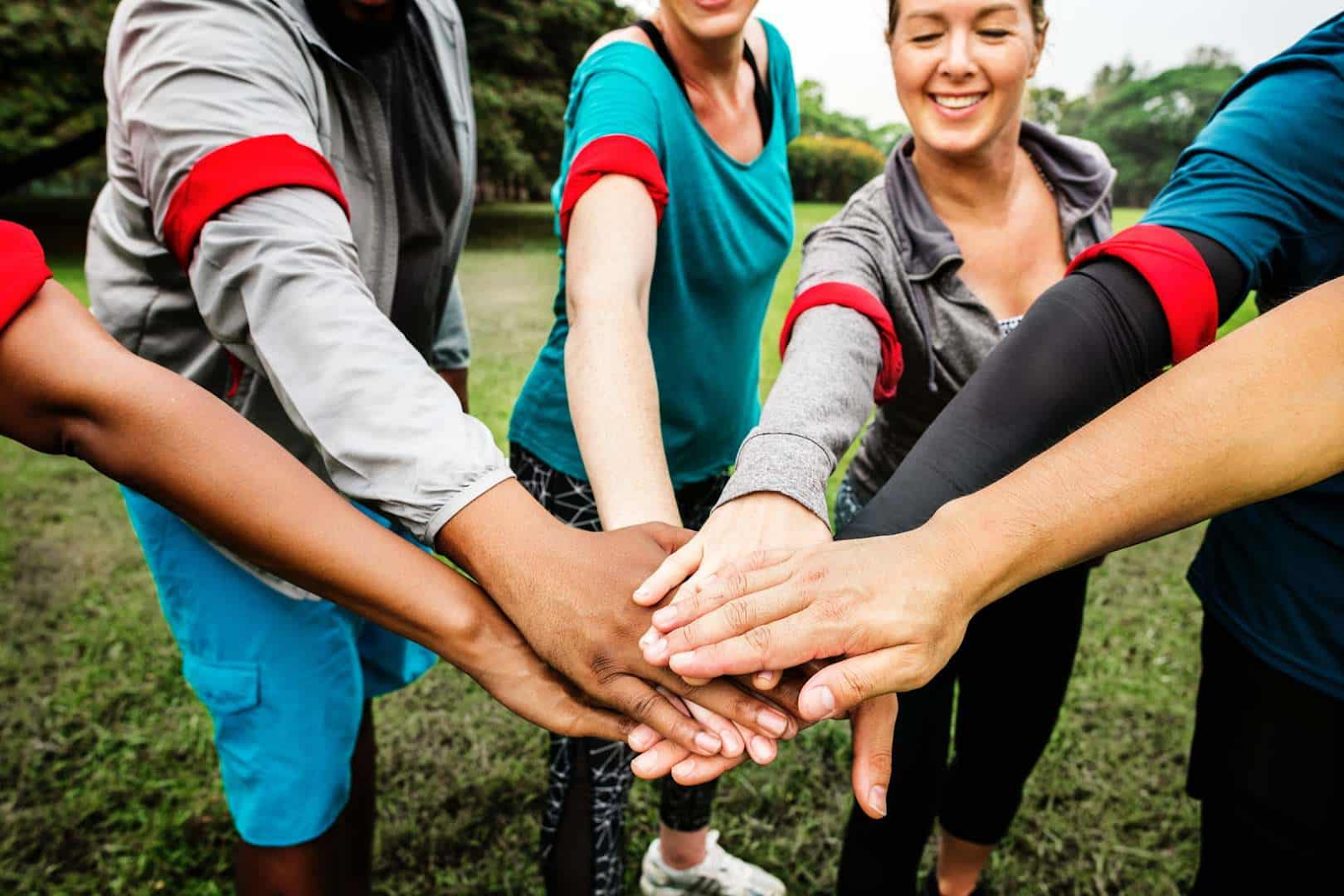 a group of people standing in a circle, uniting their hands in the middle of it