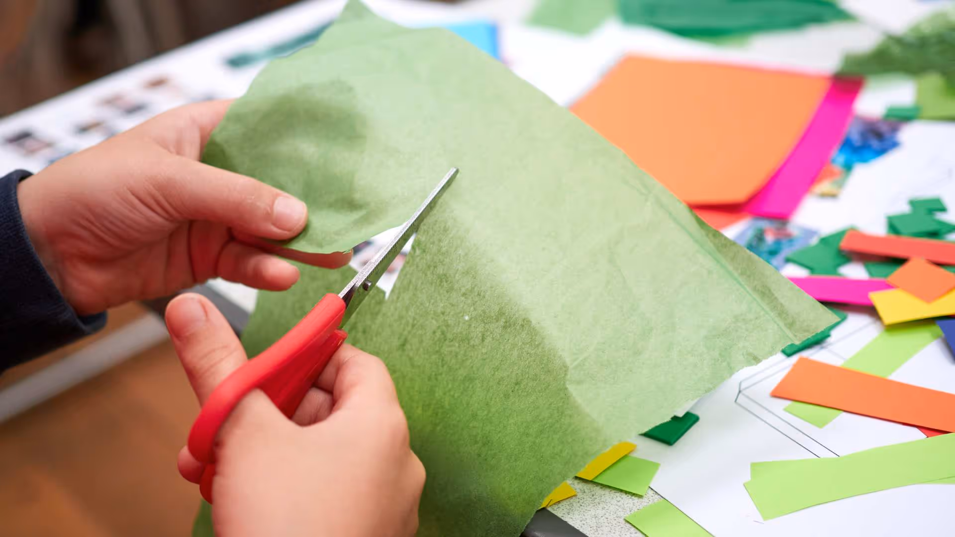 Close-up of hands cutting colorful paper during a creative team-building workshop hosted by The Craft Club.
