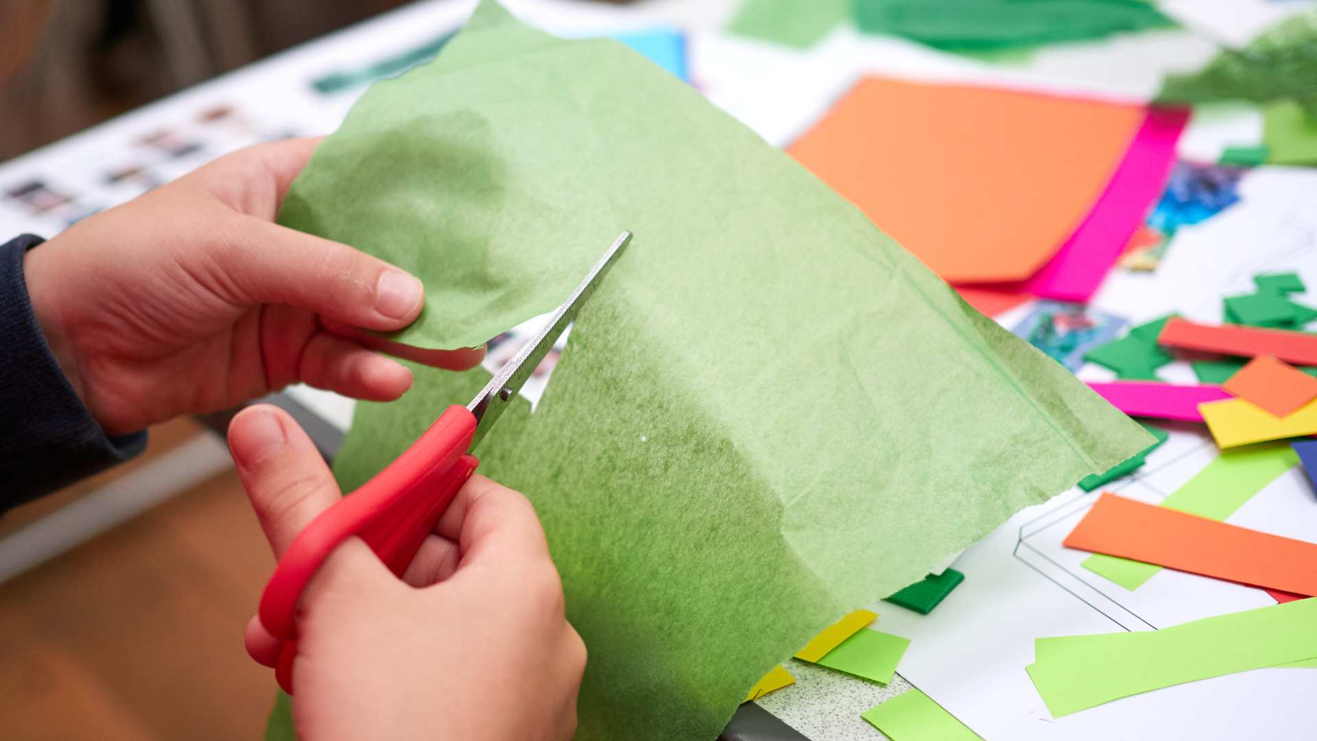 Close-up of hands cutting colorful paper during a creative team-building workshop hosted by The Craft Club.