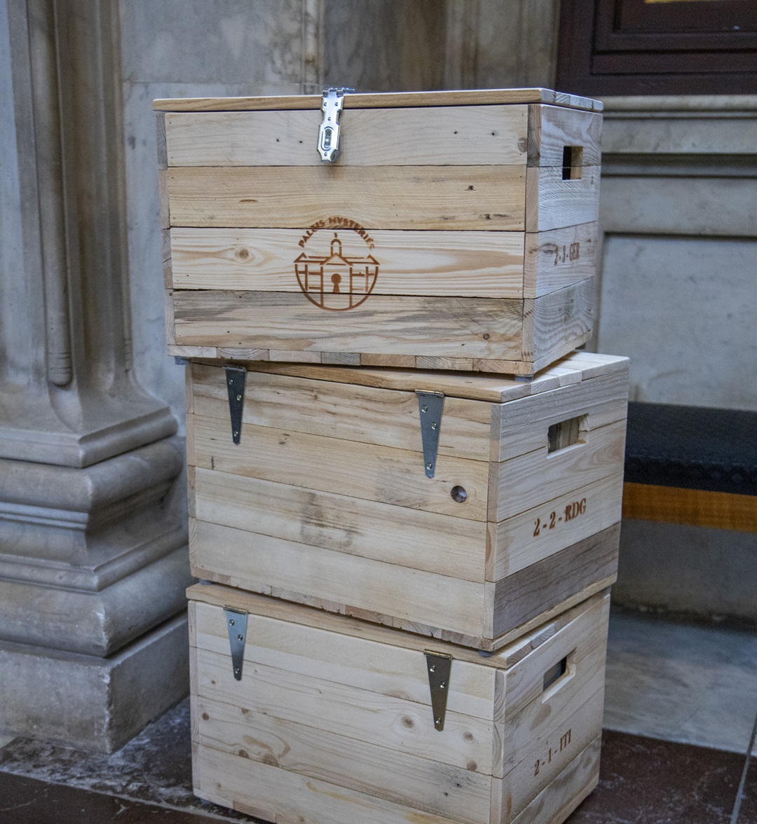 A stack of three custom-made wooden puzzle chests branded with the Palace Mysteries logo, used as portable storytelling tools by Sherlocked inside the Royal Palace.