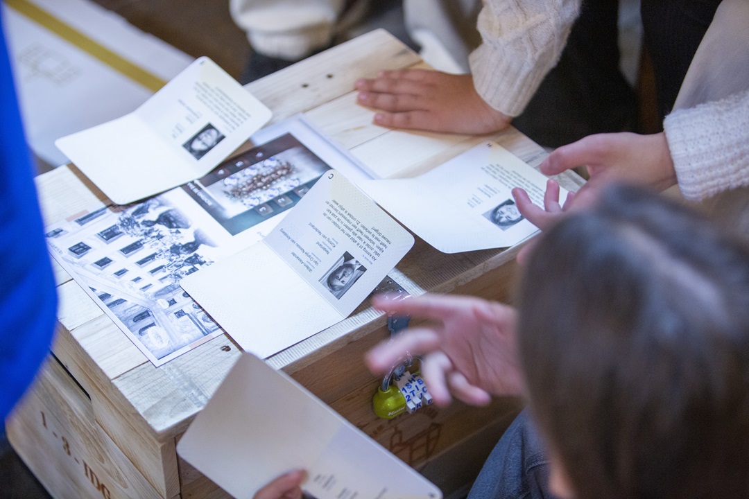 Close-up of museum interactive design materials including a wooden crate with a combination lock, historical persona passports featuring King Willem-Alexander, and tactile puzzle documents.