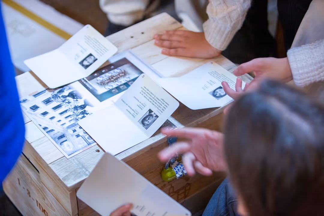 Close-up of museum interactive design materials including a wooden crate with a combination lock, historical persona passports featuring King Willem-Alexander, and tactile puzzle documents.