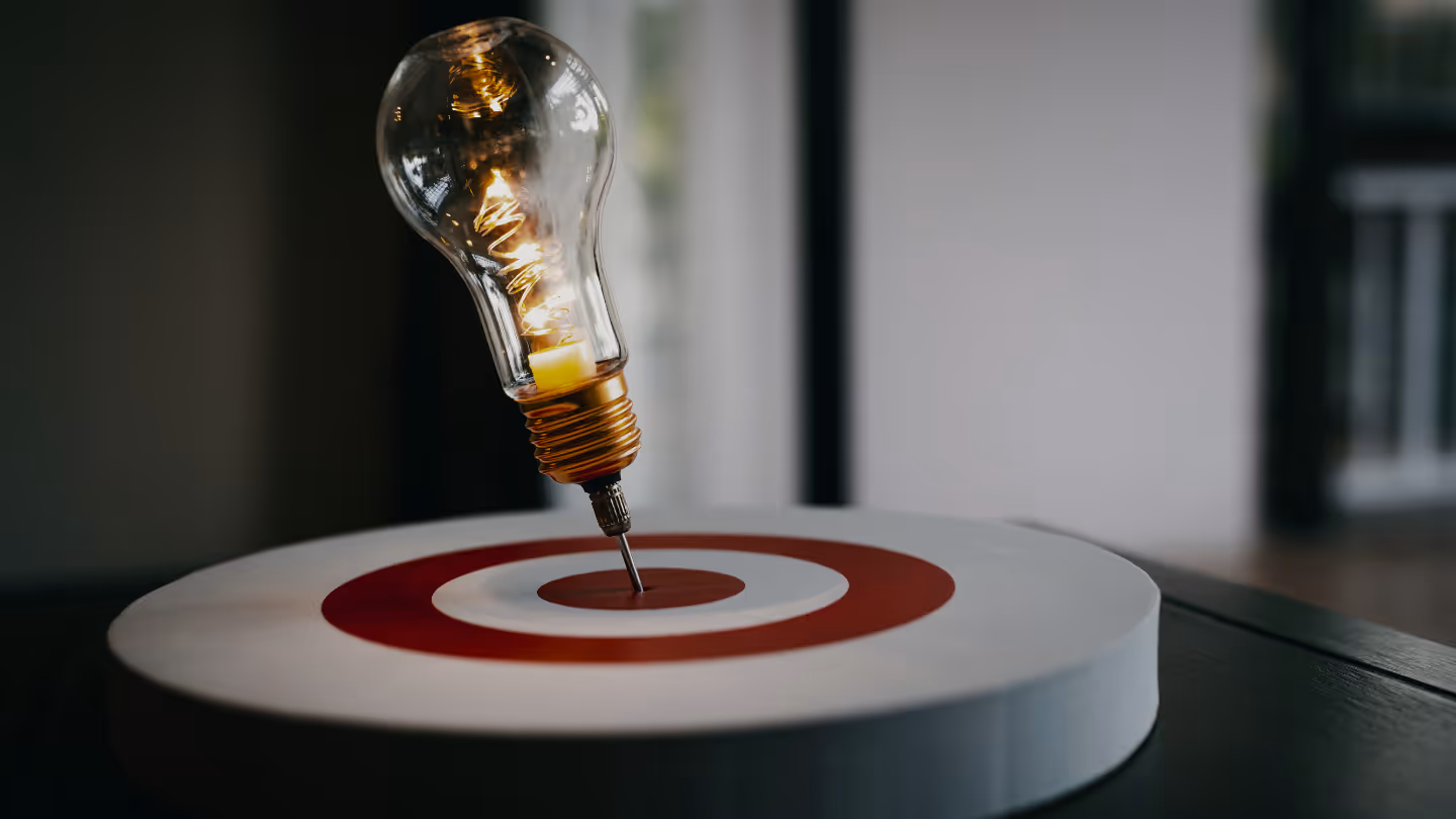 A glowing light bulb pinned to the centre of a target board, symbolising focused thinking and problem-solving