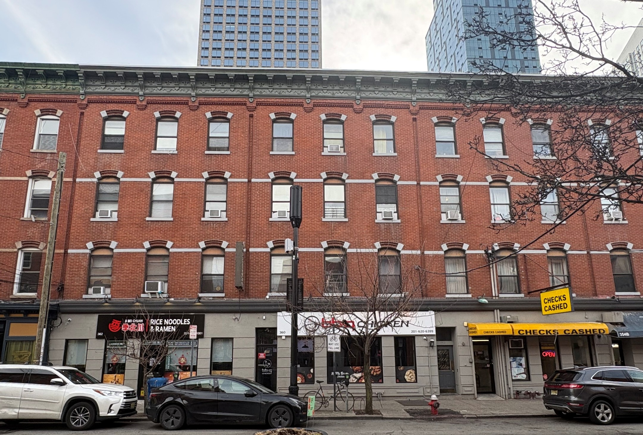 Street view of brick building with restaurants and a checks cashed shop under tall skyscrapers.