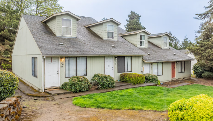 Row of pale green townhouse units with dormer windows, white and red doors, and shrubs in front.