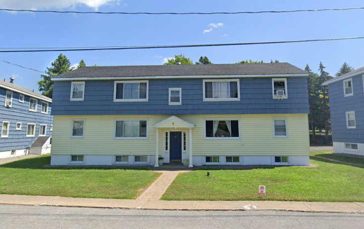 Two-story apartment building with blue upper siding and yellow lower siding, and a centered blue door.