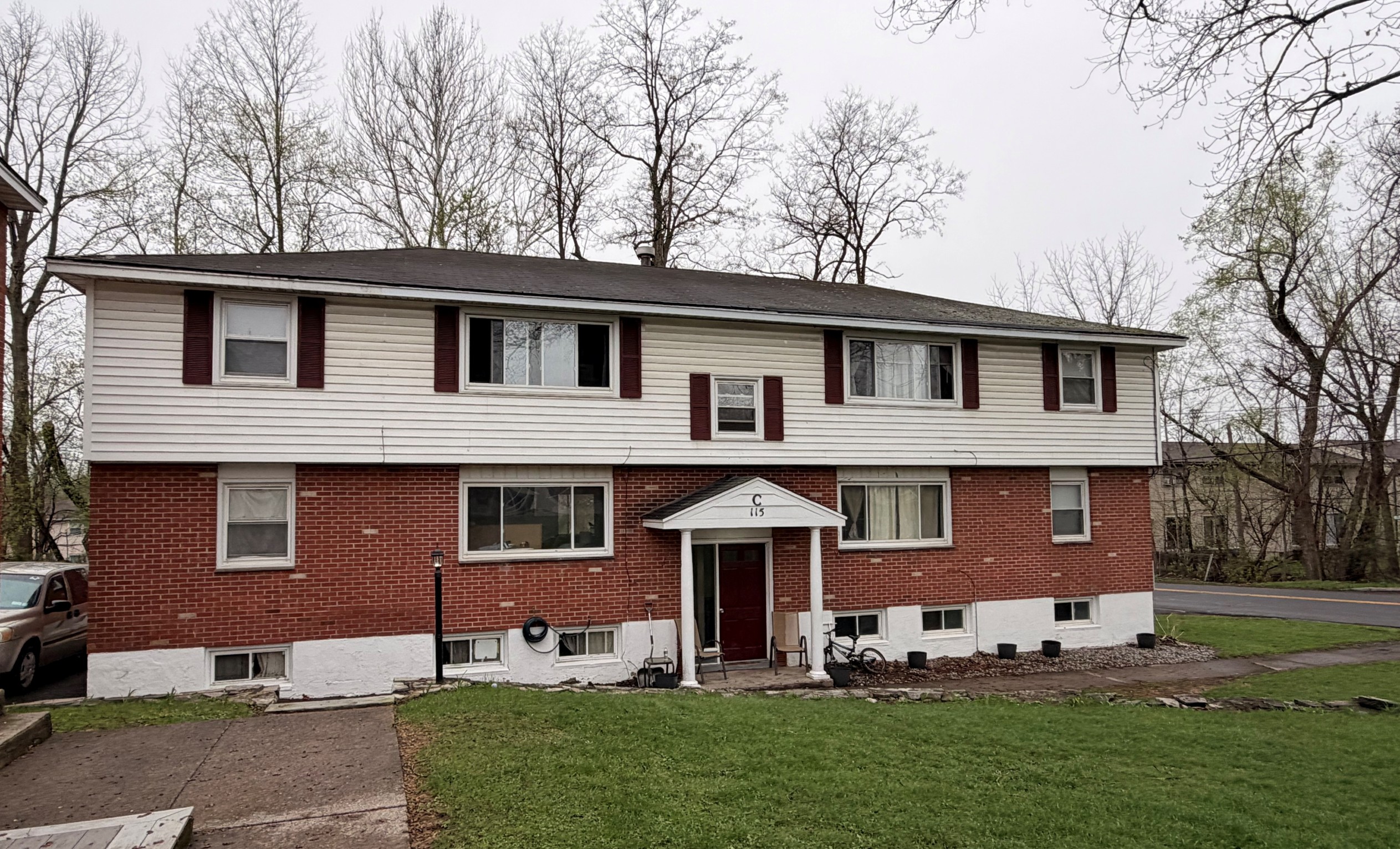 Two-story red brick and white siding residential building with maroon shutters and central porch.