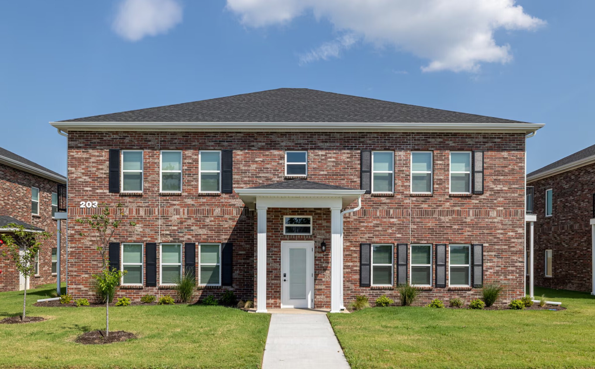Two-story brick house with white door, columns, and multiple windows with black shutters.