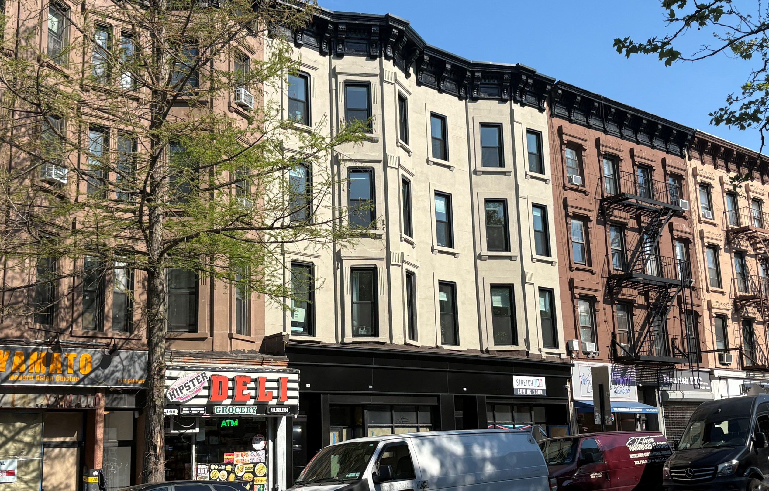 Modern three-story building with glass storefronts, balconies, and parked cars on a street.