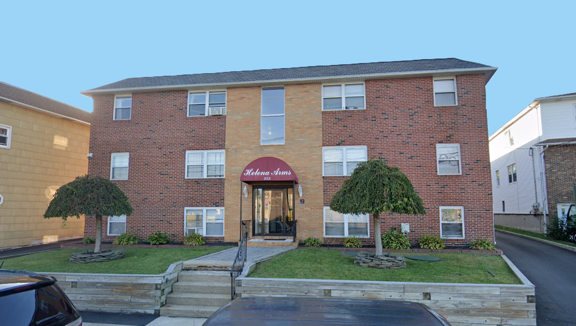 Row of two-story brick apartment buildings with brown mansard roofs under a clear blue sky.