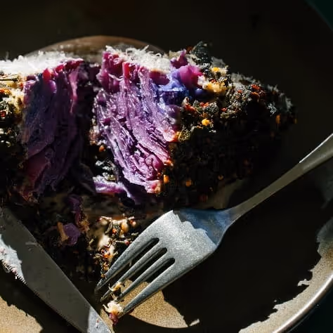 Roasted purple cabbage wedge with crispy herb crust served on a dark plate