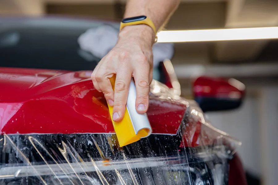 Installer applying XPEL paint protection film to a red car