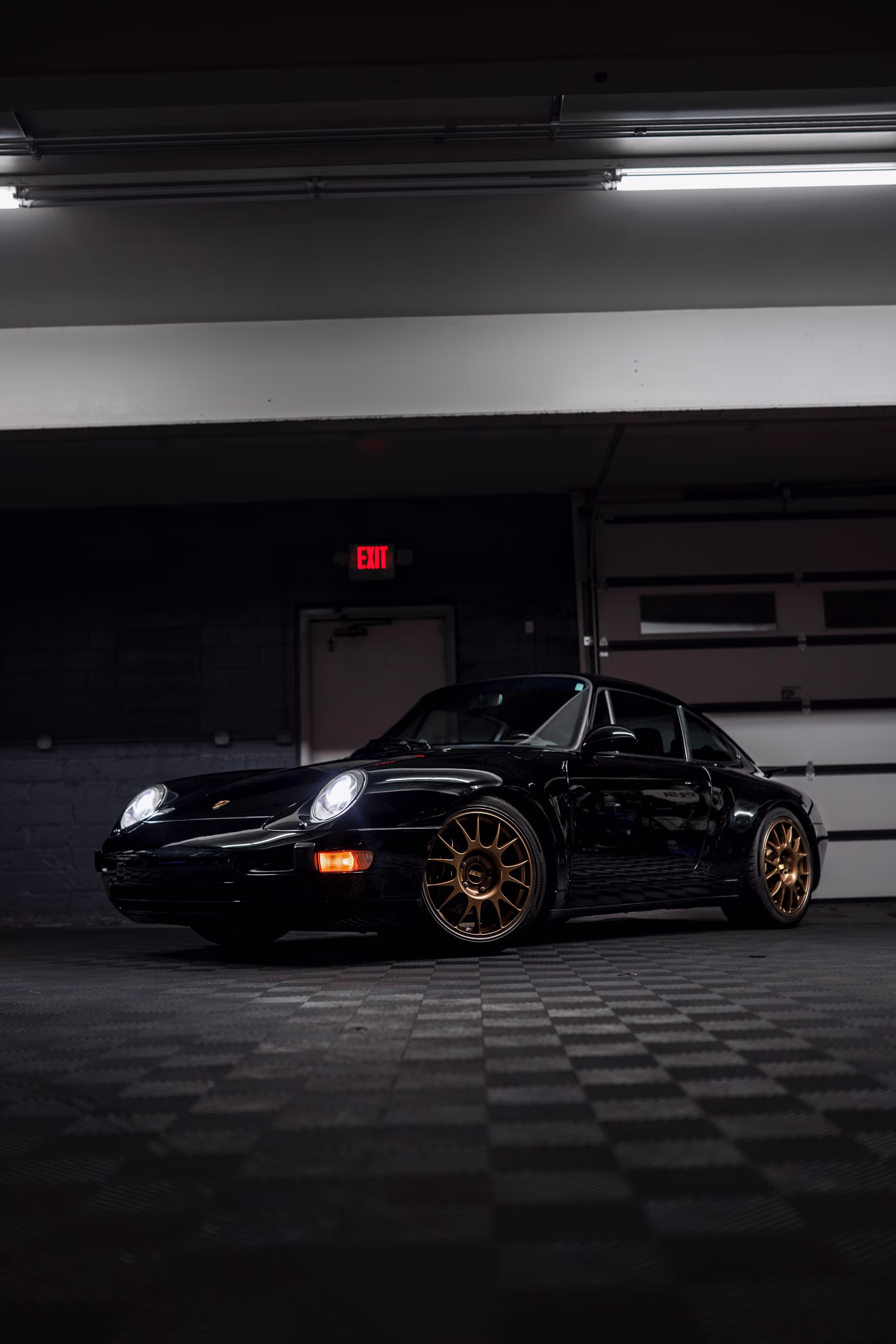 A black Porsche with gold rims parked inside a garage