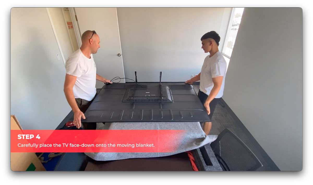 Cactus Moving workers carefully placing a large TV face-down onto a moving blanket.