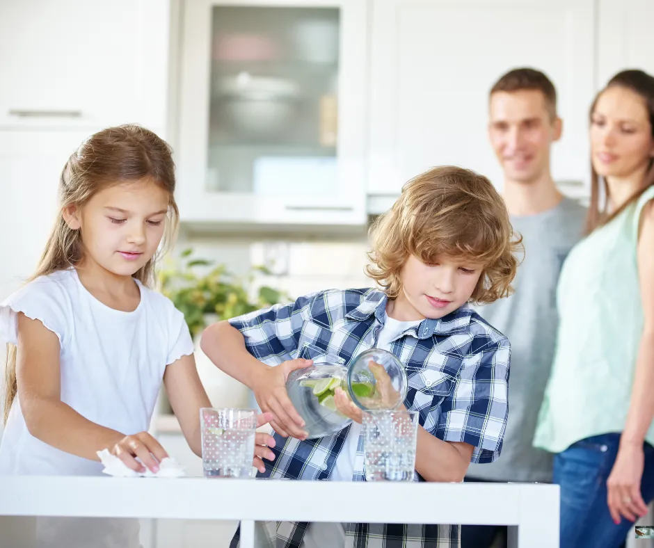 Kids pouring water into cup with parents happy in the background