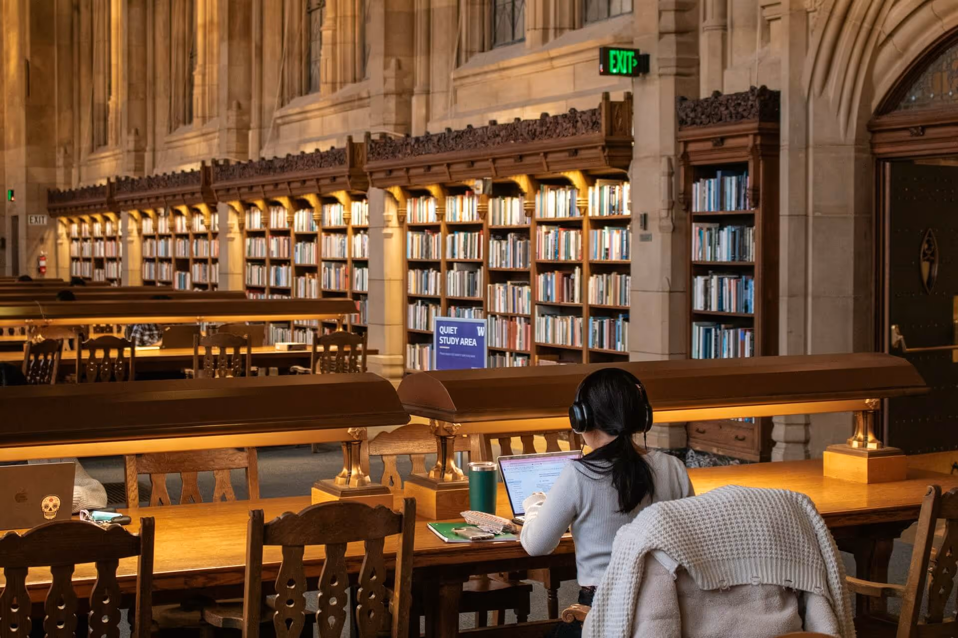 Researcher in a grand university library quietly studying at a wooden desk, using Rapidemia’s AI‑powered summarizer on a laptop to quickly review scientific research papers.