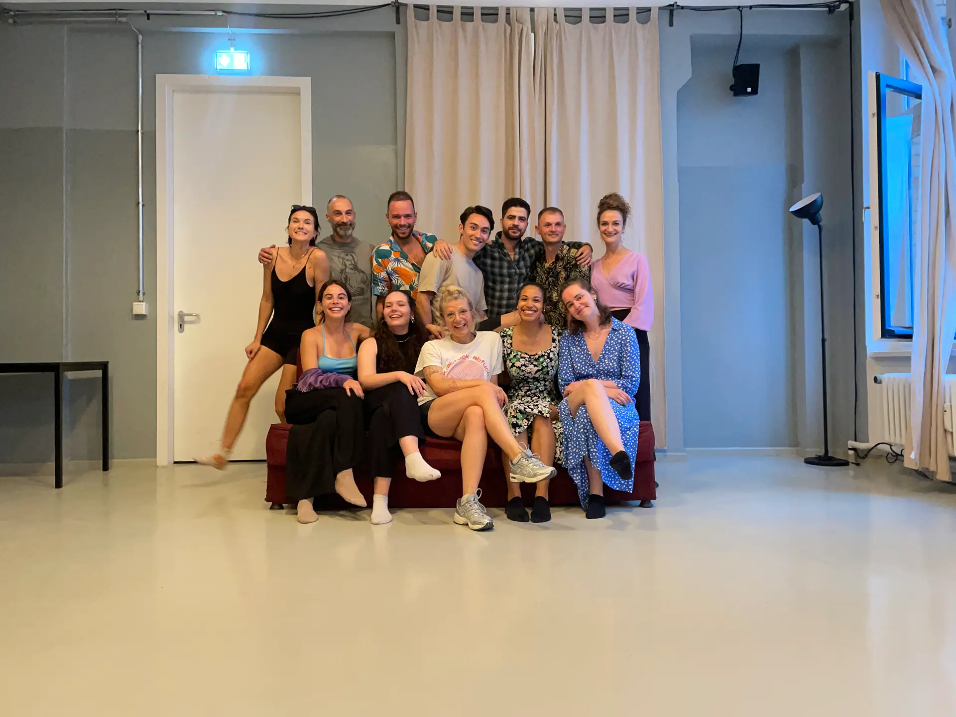 Gruppenfoto einer fröhlichen Gruppe von Kursteilnehmenden, die gemeinsam auf einem Sofa posieren und in die Kamera lächeln.