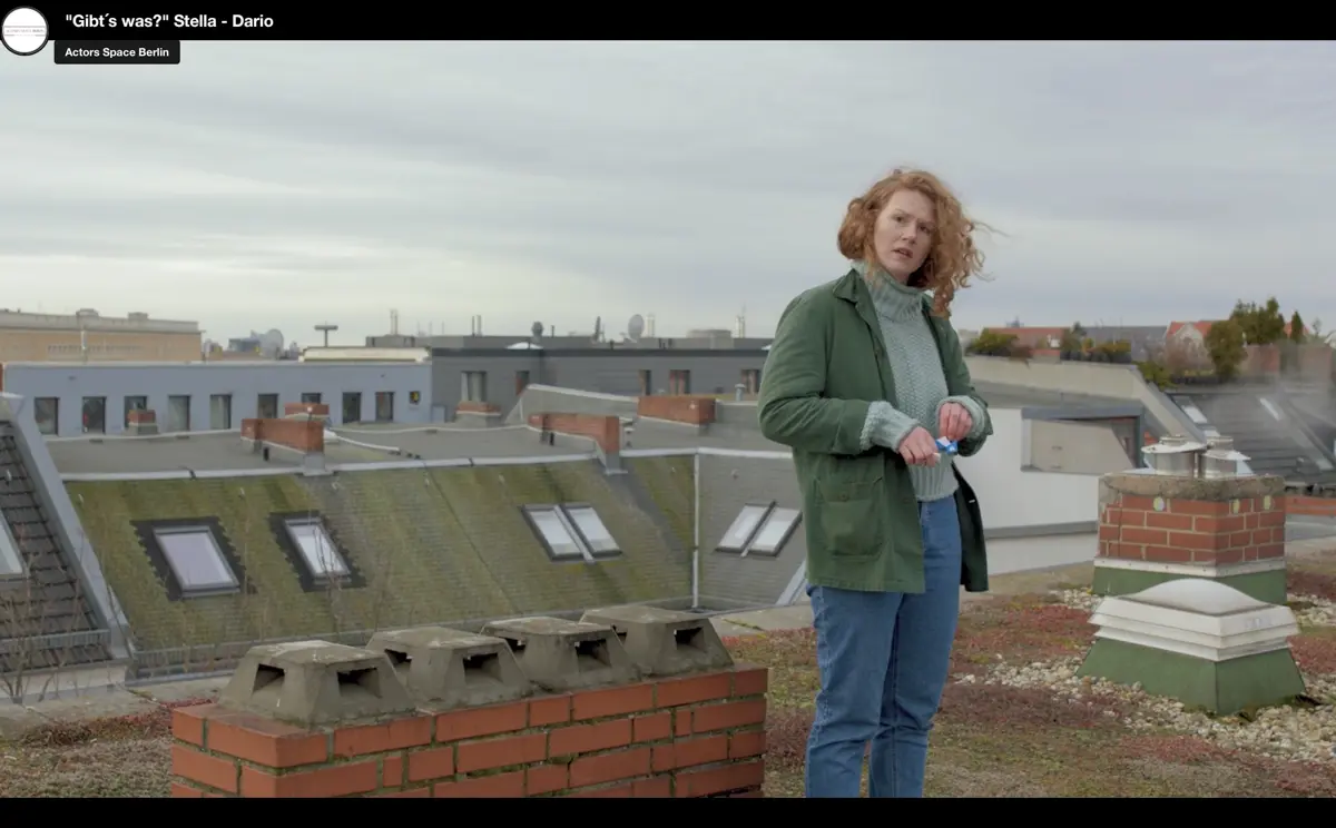 Eine Frau steht auf einem begrünten Dach und hält eine Plastikflasche in den Händen. Hinter ihr sind die Dächer benachbarter Gebäude und ein bewölkter Himmel zu sehen.