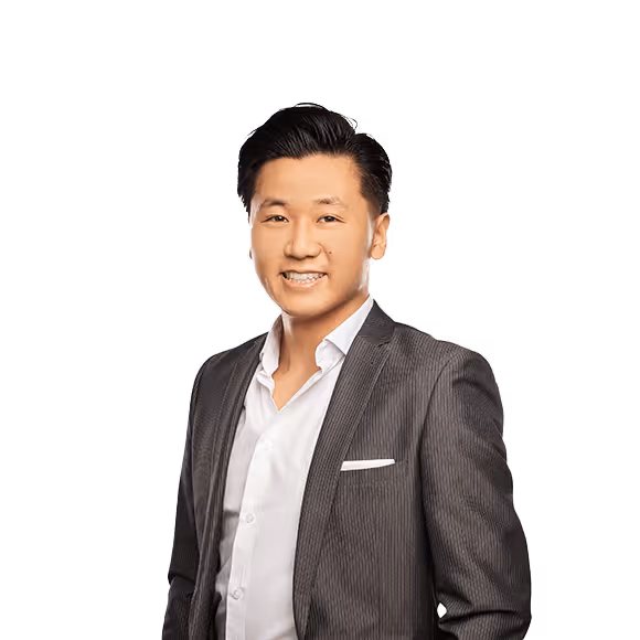 A smiling man with black hair, wearing a dark pinstripe suit jacket and a white shirt.