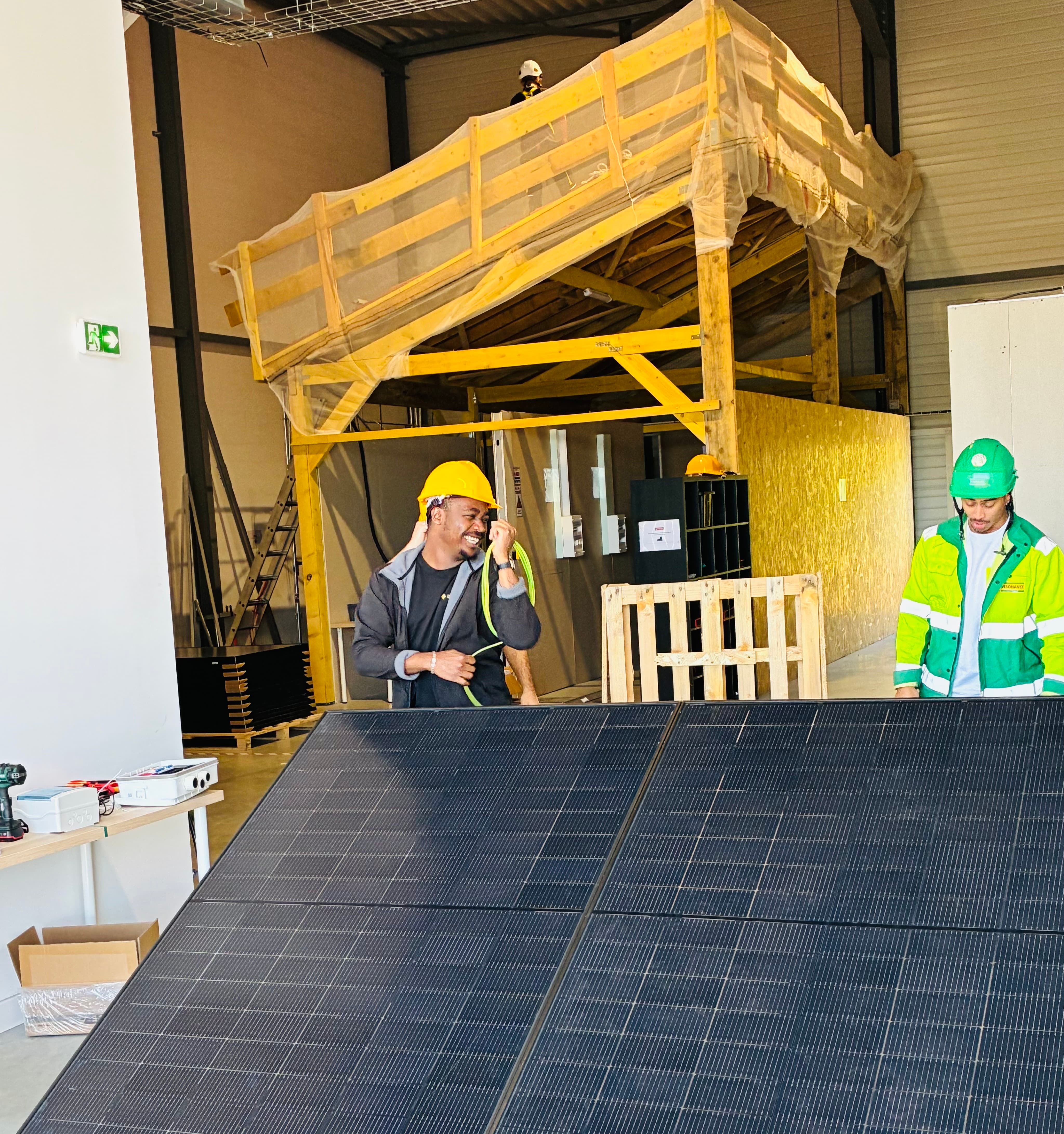 Two construction workers with helmets examining a large solar panel indoors at a work site.