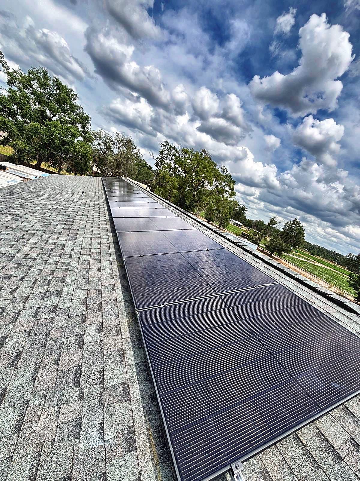 Solar array along a light gray shingle roof beneath a dramatic cloudy sky