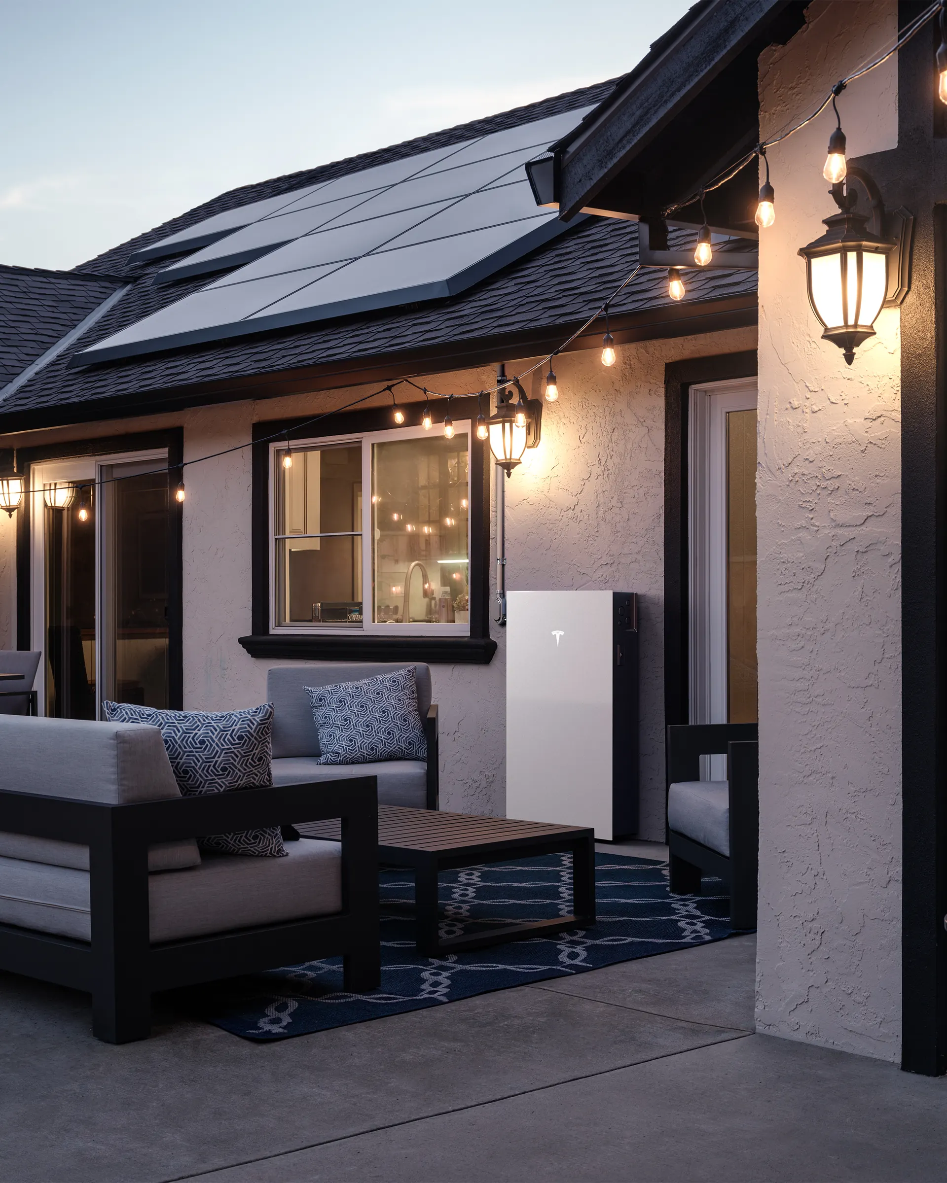 Tesla Powerwall 3 on a covered patio with outdoor seating at dusk
