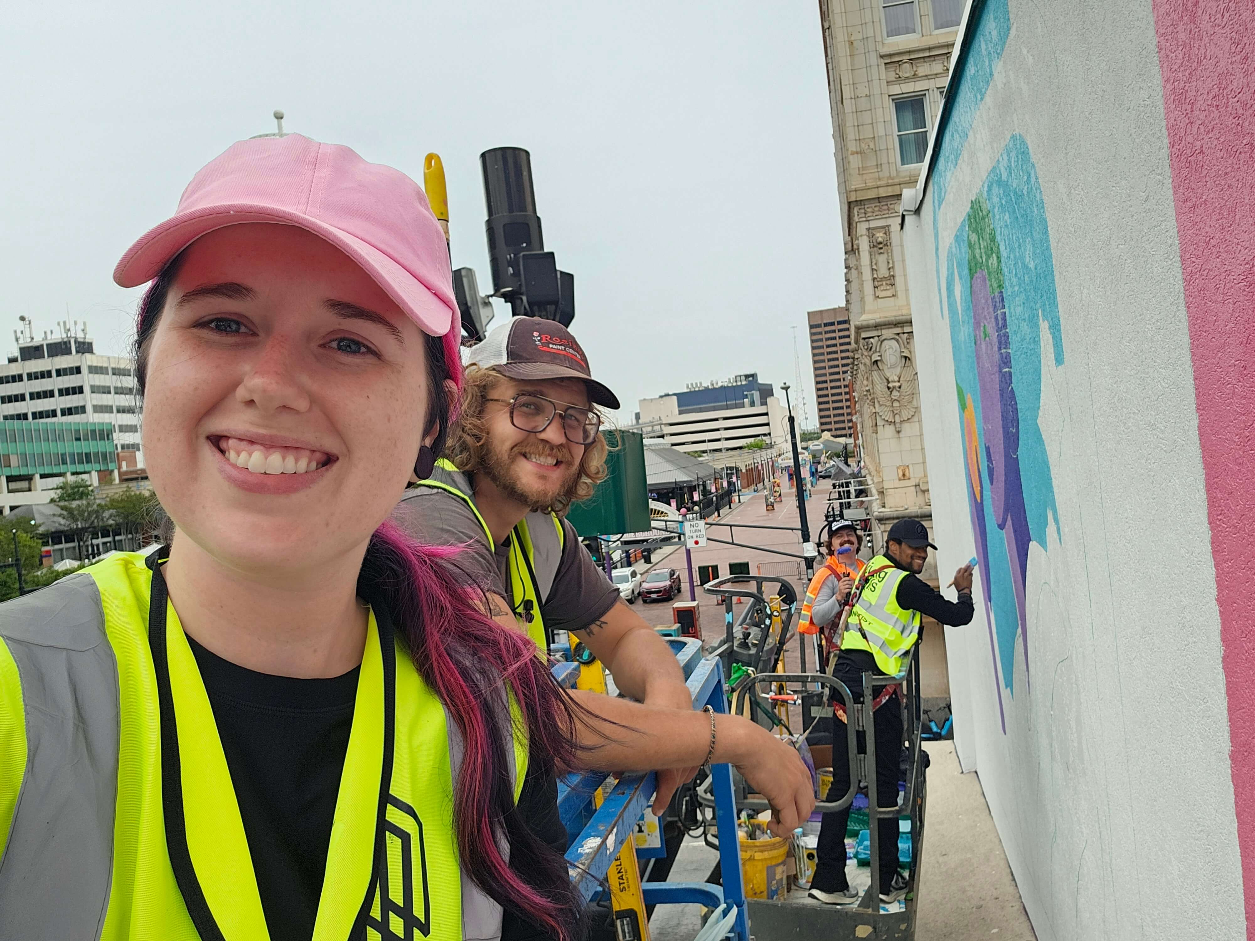 Brianna Gardocki and assisting artists working on a South Downtown Atlanta mural with Living Walls, with the mural and lift equipment visible.