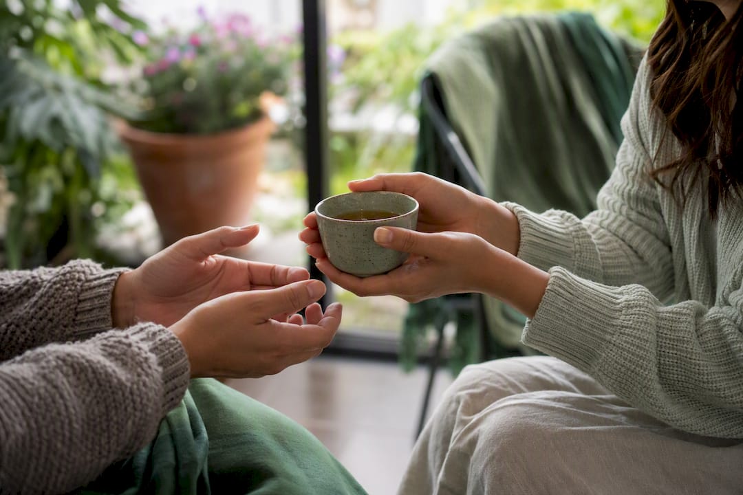 Hands passing tea cup in peer support setting